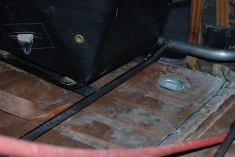 1982 Ford Bronco - Close-up of the interior showing a black seat base and roll cage tubing, with a rusty floor pan visible.