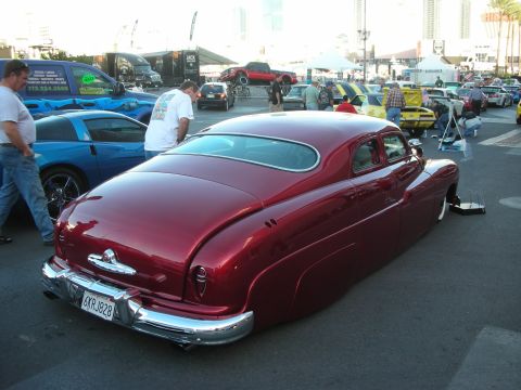 1998 Ford Crown Victoria - candy-red chopped lead-sled-style custom car sits lowered in an outdoor lot show, seen from the rear three-quarter with a California plate.