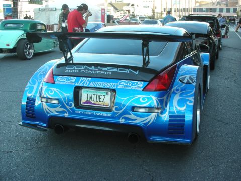 1998 Ford Crown Victoria - blue Nissan 350Z with white tribal-style graphics, wide body, and a tall rear wing parked in an outdoor show lot.