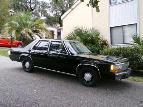 1991 Ford Crown Victoria - A black sedan is parked on a street with a red SUV in the background.