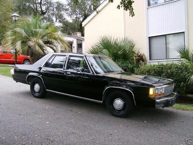 Black sedan parked on asphalt, front quarter view. Chrome trim, hubcaps visible. Red SUV in background