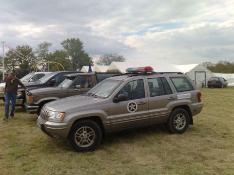 1991 Ford Crown Victoria - A Jeep Grand Cherokee, possibly a police or security vehicle, is parked in a grassy area with tents and other vehicles in the background.