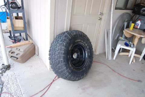 1982 Ford Bronco - A single off-road tire is shown in front of a garage door, with various tools and equipment in the background.