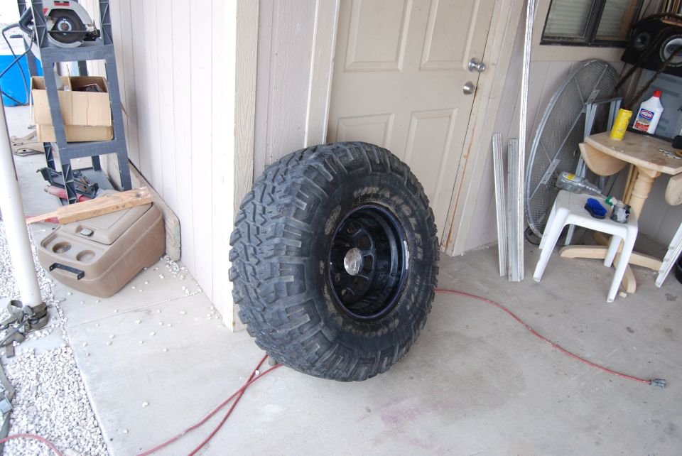 Large off-road tire with black rim leaning against a white door