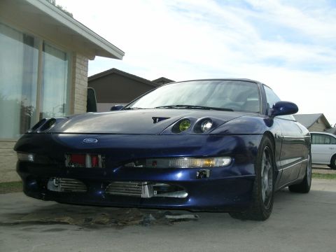1995 Ford Probe - A modified blue Ford Probe from the mid-1990s is shown from the front-left angle, parked outside a residential building.