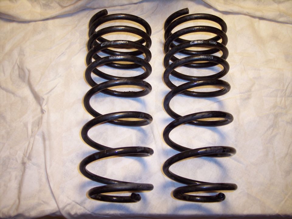 Two black coil springs are laid out on a white cloth. Part numbers are visible on the springs