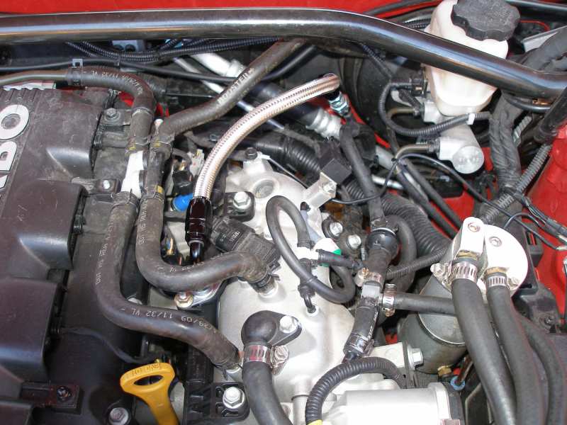 Engine bay with fuel lines, hoses, and brake fluid reservoir visible. Some hoses have text on them