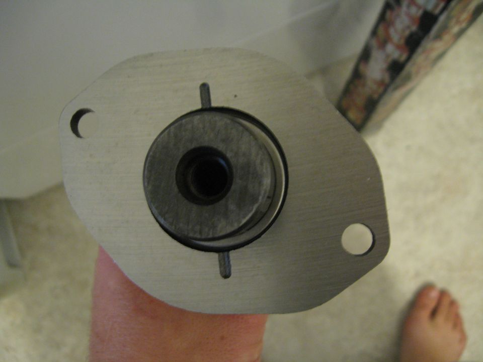 Close-up of a metal part with a circular component and two bolt holes, held by a hand