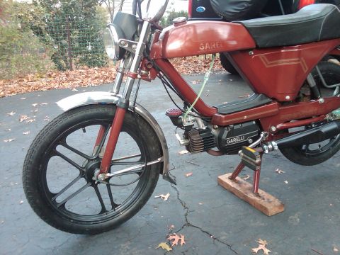 1981 Garelli Rally Sport - Side view of a red Garelli moped with a black seat and wheels, parked outdoors.