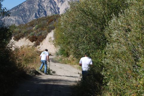 1996 Ford Bronco - Two men walk up a dusty mountain road surrounded by trees and brush, with a large mountain in the background.