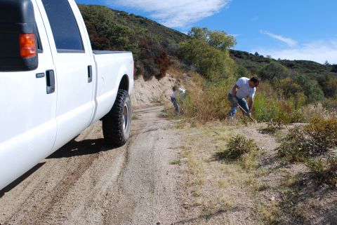 1996 Ford Bronco - A white pickup truck is parked on a dirt road while two people work on the side of the hill.