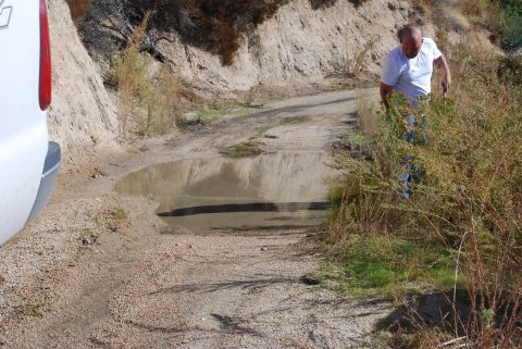 1996 Ford Bronco - A white SUV's rear quarter panel is visible on a rough dirt road, with a man walking in the background.