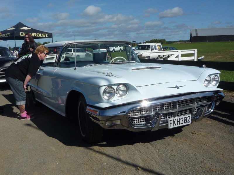 Light blue 1958 Ford Thunderbird convertible with a woman looking at it. License plate FKH382