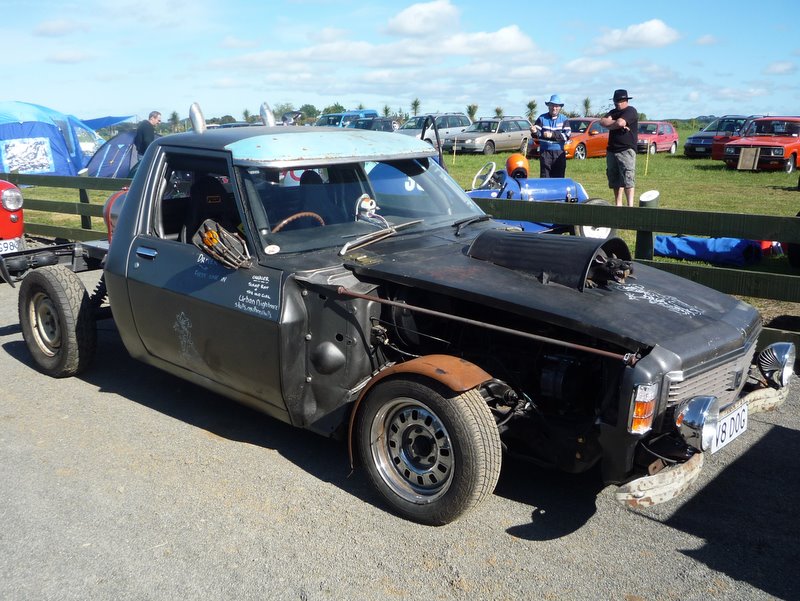 Heavily modified pickup truck with custom hood scoop, exposed engine components, and mismatched fenders. License plate reads 'V8 DOG'