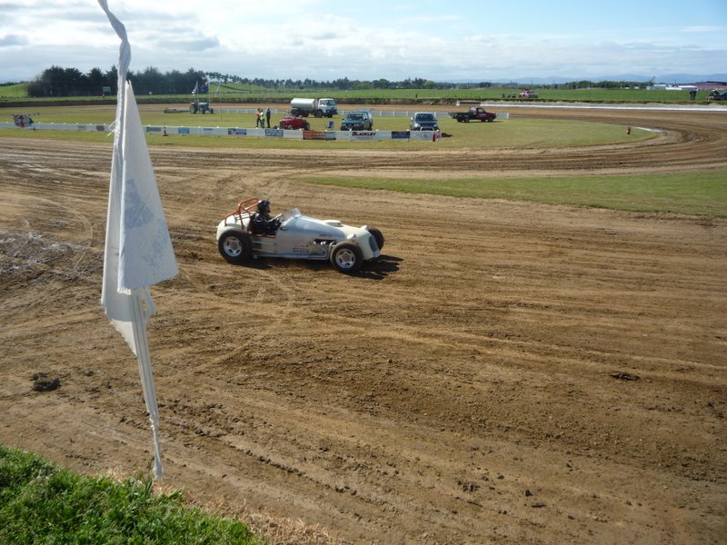 White open-wheel speedway car with orange-helmeted driver on a dirt oval track