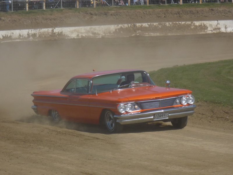 Orange 1959 Pontiac Bonneville driving on a dirt track, kicking up dust