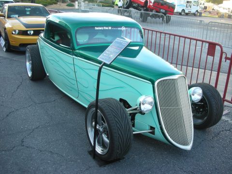 1998 Ford Crown Victoria - green hot rod three-window coupe with ghost flames sits outdoors on a stand, with a Factory Five placard in the windshield.