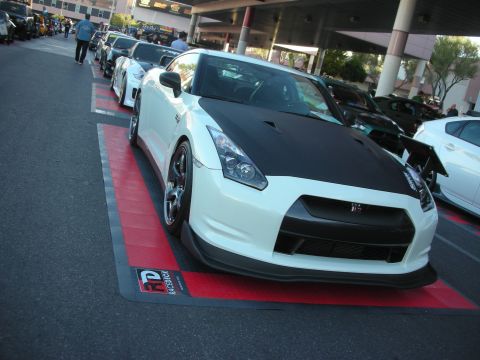 1998 Ford Crown Victoria - white Nissan GT-R with a black carbon-fiber hood sits front three-quarter on a red display pad in an outdoor show lineup.