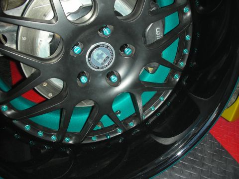 1998 Ford Crown Victoria - Close-up of a black multi-spoke wheel with teal-anodized hardware and a teal inner barrel mounted over a slotted brake rotor.