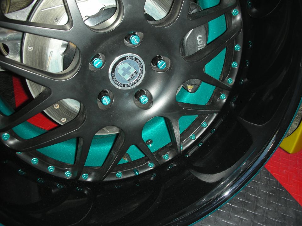 Close-up of black multi-spoke HRE-style wheel with teal accents over a brake rotor