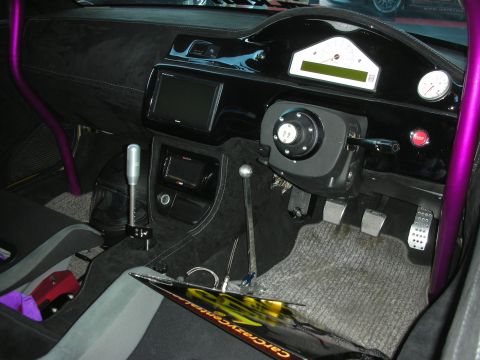 1998 Ford Crown Victoria - stripped race-style car interior with a purple roll bar, hydraulic handbrake lever, aluminum pedals, digital dash, and center screen.
