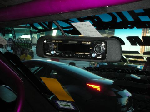1998 Ford Crown Victoria - windshield-mounted rearview mirror with a built-in stereo head unit, viewed from inside a car overlooking a purple-and-black vehicle at an…
