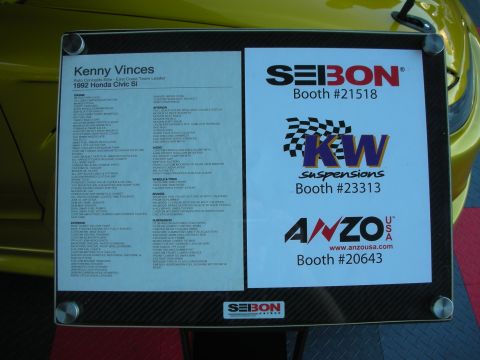1998 Ford Crown Victoria - carbon-fiber-framed display board listing build specs for owner Kenny Vinces beside Seibon, KW Suspensions and Anzo sponsor logos and booth…