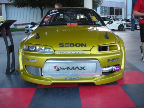 1998 Ford Crown Victoria - Front view of a yellow modified coupe with an exposed front-mount intercooler, Seibon-branded vented hood and sponsor decals on a red-and-b…