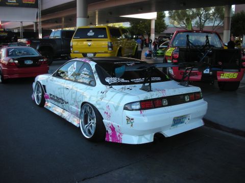 1998 Ford Crown Victoria - Rear three-quarter view of a white sport coupe with paint-splatter graphics, big rear wing and aftermarket wheels parked in a covered show…