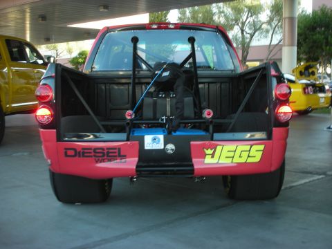 1998 Ford Crown Victoria - Tail-on view of a red-and-black drag pickup with open tailgate revealing an interior roll cage and parachute, wearing Diesel World and Jegs…