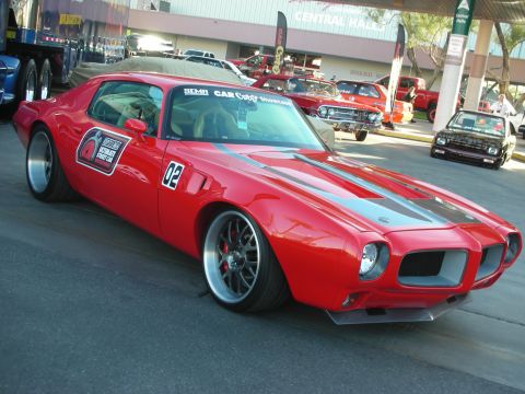 1998 Ford Crown Victoria - red second-gen Pontiac Firebird pro-touring coupe with race number 02, hood-mounted decals and staggered wheels at an indoor SEMA-style sho…