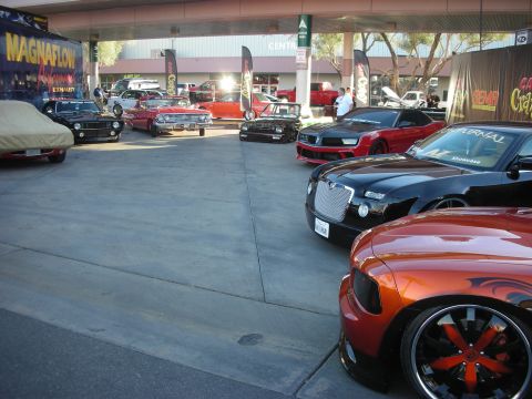 1998 Ford Crown Victoria - lineup of customized cars under an outdoor canopy, including classic muscle cars and a copper-orange Dodge Charger on large black wheels.