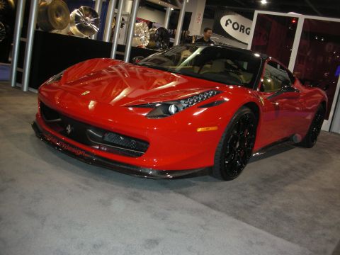 1998 Ford Crown Victoria - Front three-quarter view of a red Ferrari 458 Italia on gloss-black wheels with carbon front lip, displayed at a wheel-vendor booth.