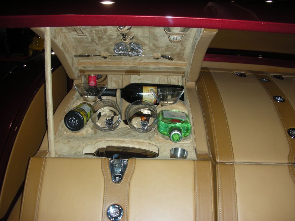 Open in-vehicle bar console with wine bottle, glasses and tan leather trim