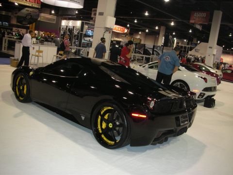1998 Ford Crown Victoria - Rear three-quarter view of a black Ferrari 458 with yellow brake calipers and wheel accents, parked among other cars at a crowded indoor sh…