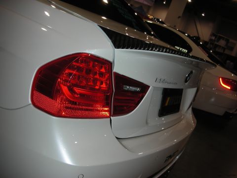 1998 Ford Crown Victoria - Close-up of a white BMW sedan's rear corner with a glowing LED taillight, decklid spoiler and trunk badge under show lighting.
