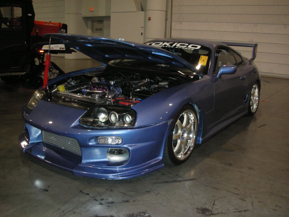 Blue Toyota Supra with open hood showing engine bay and rear wing indoors