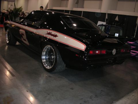 1998 Ford Crown Victoria - black first-generation Chevrolet Camaro with a white side stripe and a red number 3, on polished wheels at an indoor car show.