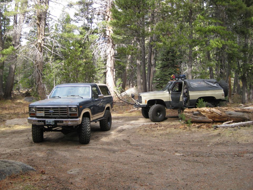 1980 Ford Bronco being towed by a lifted Chevrolet K5 Blazer in a wooded area