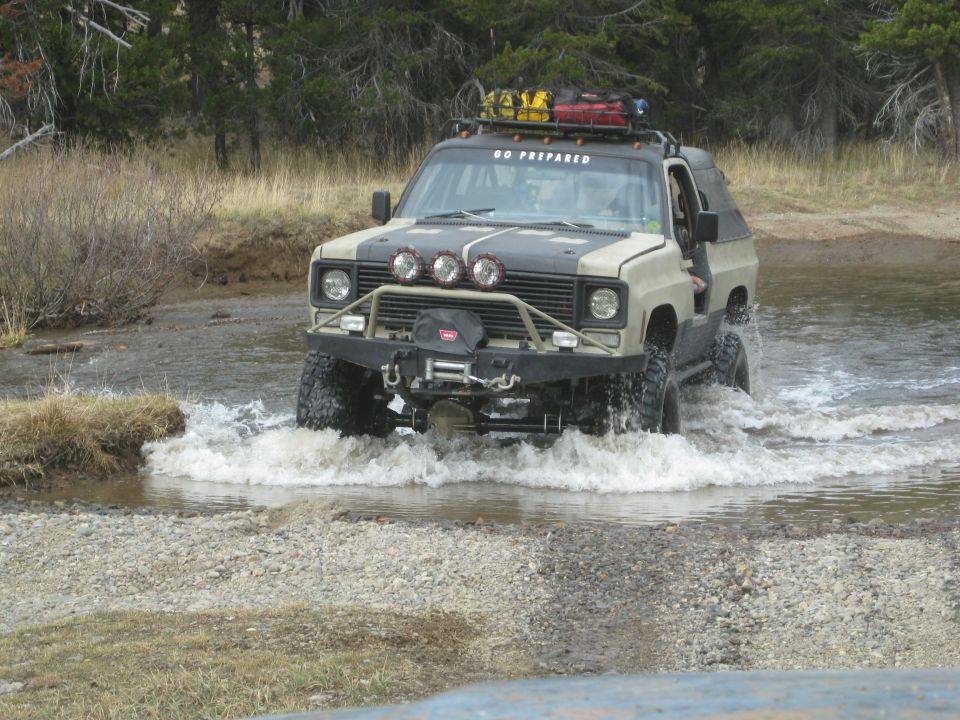 Tan and grey off-road SUV with winch and roof rack driving through water