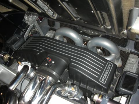 1998 Ford Crown Victoria - black intake manifold labeled FORD GT sits atop the engine, with silver exhaust headers and polished pipes visible below.