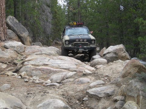 1986 Ford Bronco - Off-road vehicle tackling a challenging rocky trail in a wooded area.
