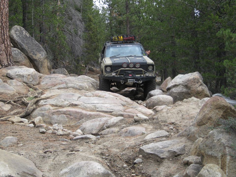 Modified off-road SUV with roof rack and winch driving over large rocks