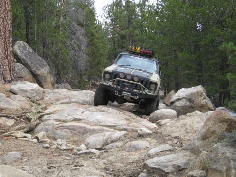 1986 Ford Bronco - This modified SUV is tackling a challenging rocky path in a forested area.