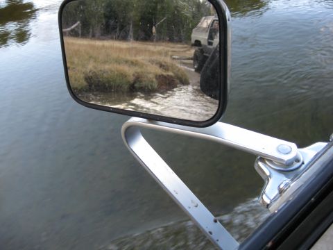 1986 Ford Bronco - Reflection in the side mirror shows a truck with large tires navigating a grassy shoreline.