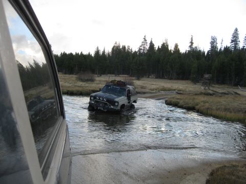 1986 Ford Bronco - Two off-road vehicles navigate a stream in a wooded area.