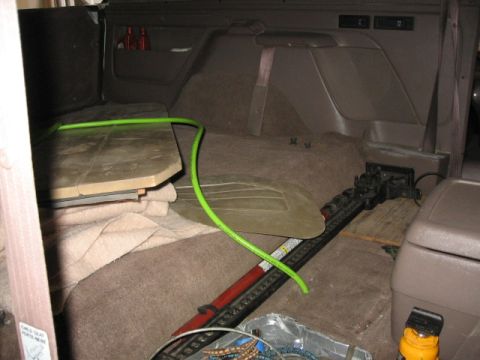 1995 Ford Bronco - The interior of a vehicle shows a jack and a green hose, with a folded seat in the background.
