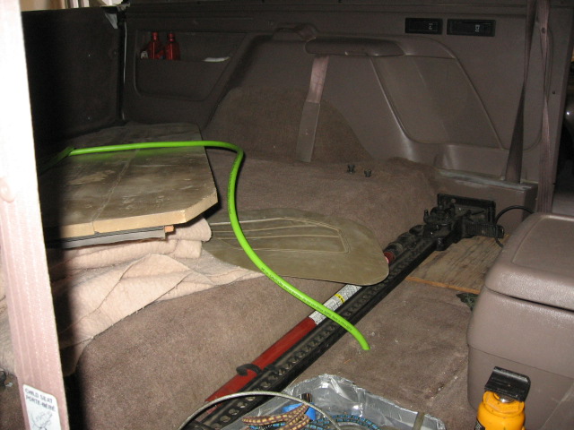 SUV cargo area with tan carpet, green hose, blanket and scattered tools