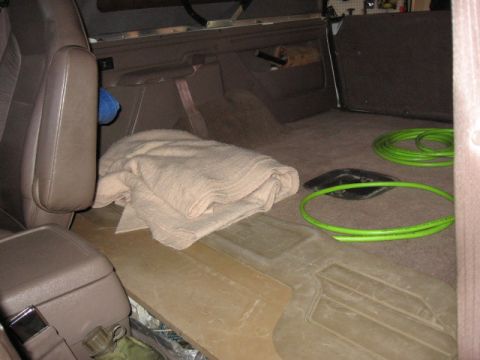 1995 Ford Bronco - The interior cargo area of a vehicle contains a folded blanket and two green hoses coiled on the floor.