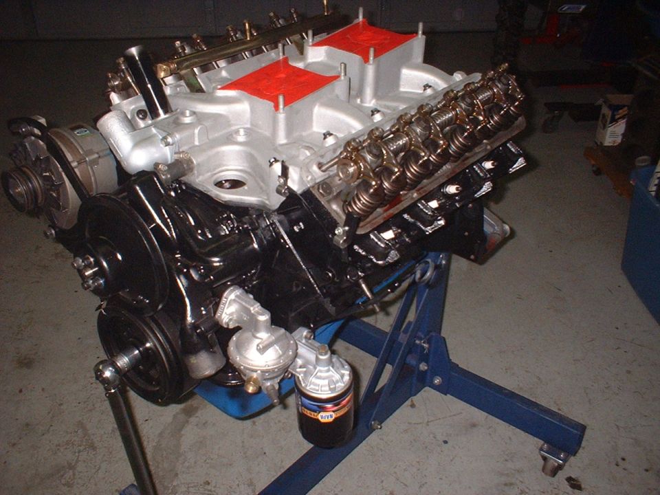 Engine on a blue stand, with black block and silver intake manifold with red covers
